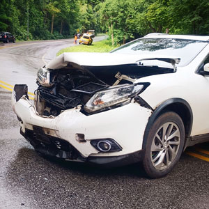 Front of a white car heavily damaged in an accident, parked on a wet road.